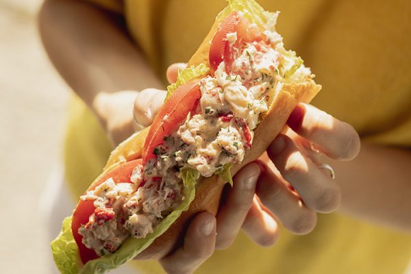Lobster Roll in hand of women wearing yellow jumper